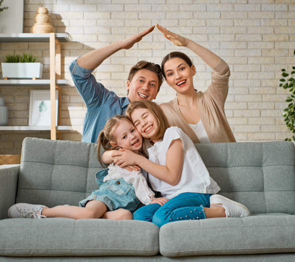 young happy family creating a house frame with arms whilst two young children sit on the sofa